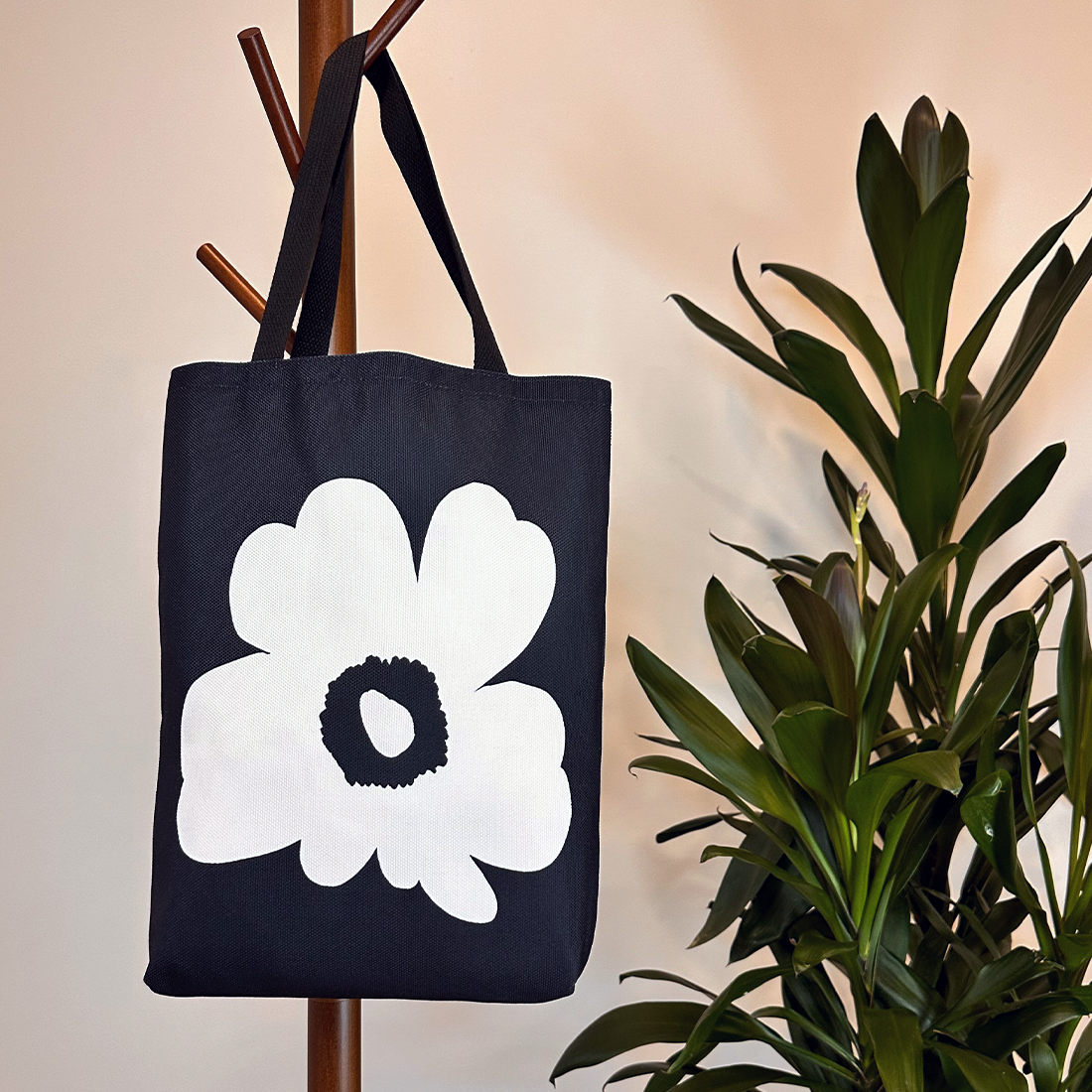 Black tote bag with white floral design, hanging on a wooden rack, adding a touch of elegance to its surroundings.