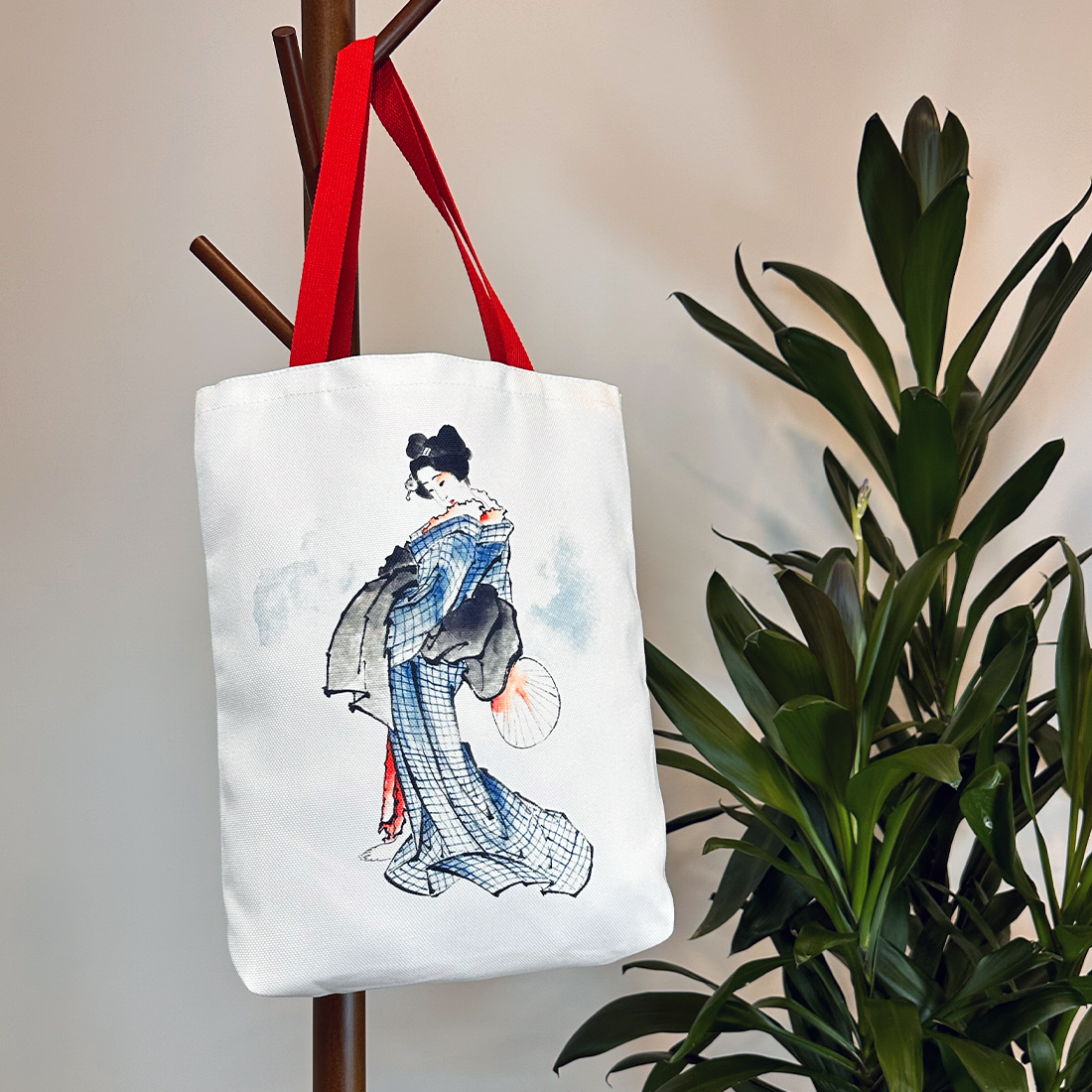 Lifestyle image of a geisha-themed white tote bag with red straps, hanging on a coat rack.