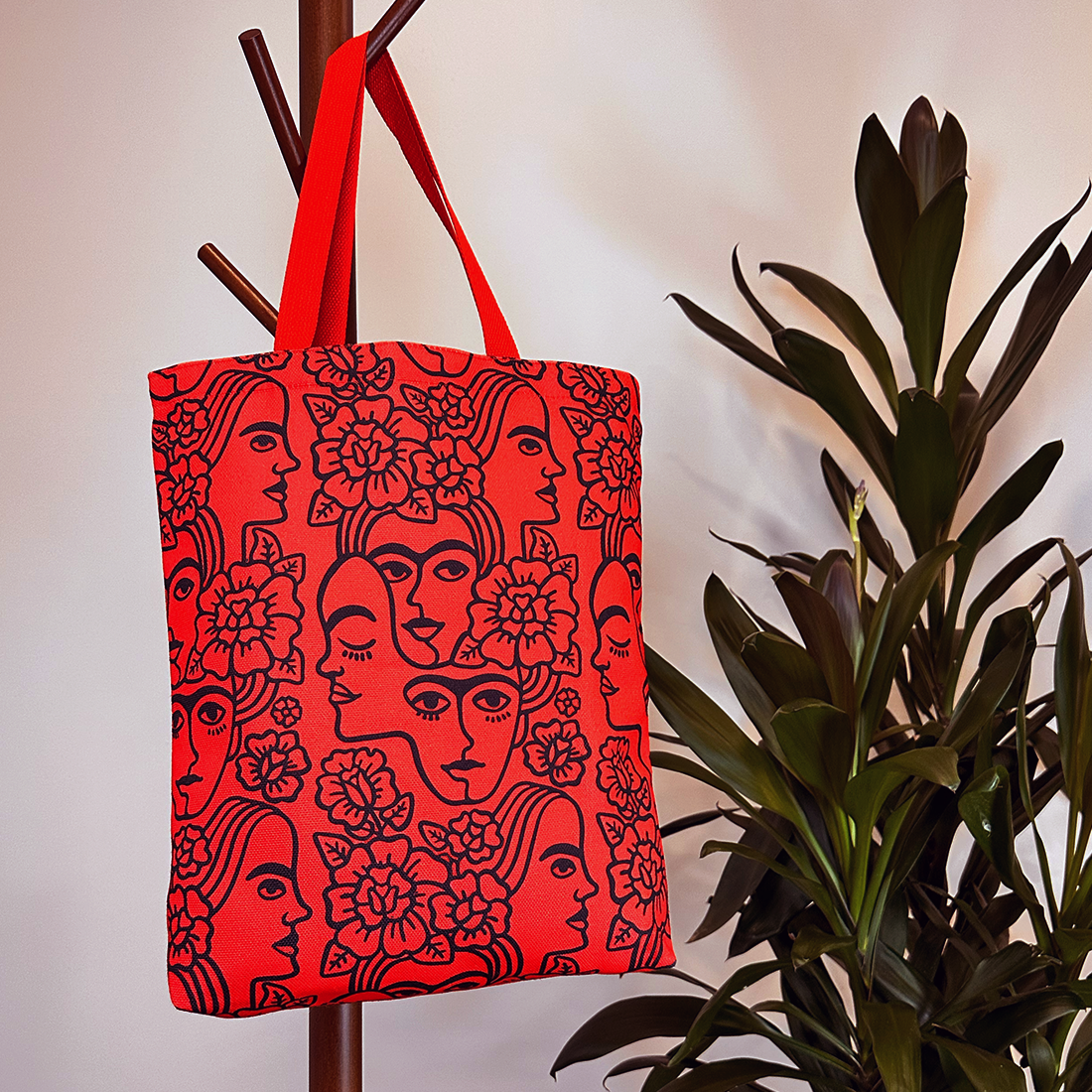 Lifestyle image of a red tote bag with bold black patterns hanging on a coat rack.