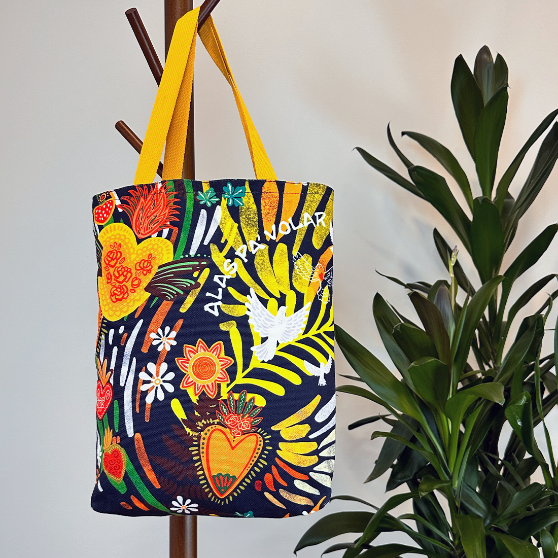 Lifestyle shot of a tote bag on a coat rack with bold botanical motifs and a yellow strap, adding a cheerful touch.